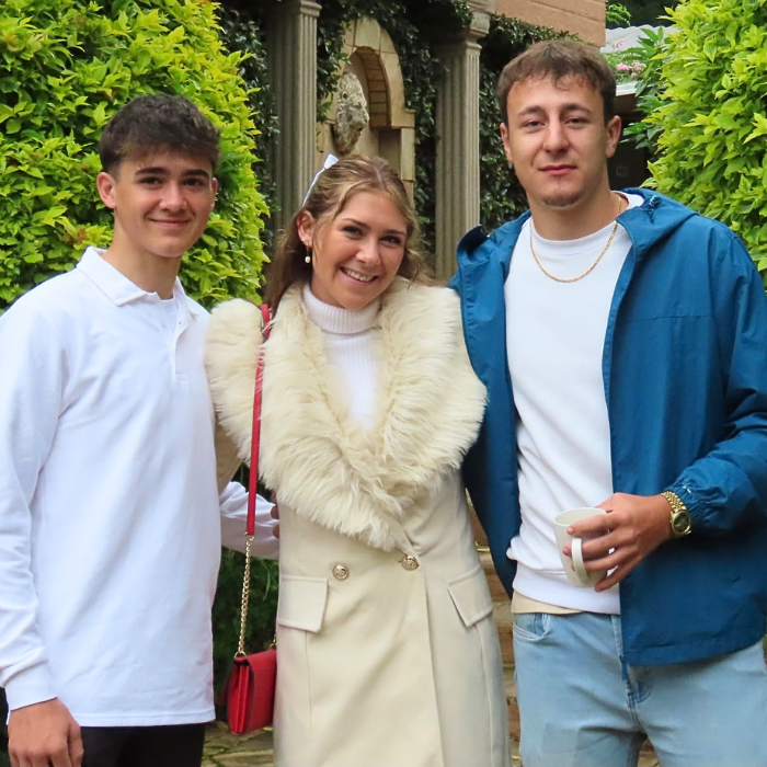 Two young men and a woman smiling together in a green garden courtyard.