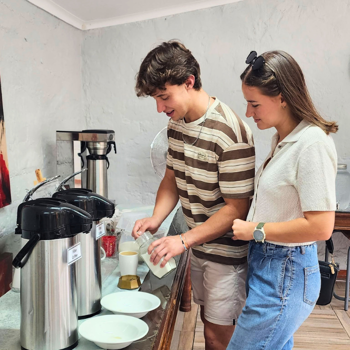 A young man and woman standing together pouring coffee from urns onto a counter.