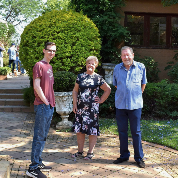 Three church members chatting together on a paved courtyard surrounded by garden greenery.