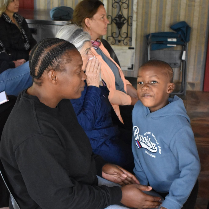 A woman gently comforting a seated mother and young boy indoors during a church gathering.