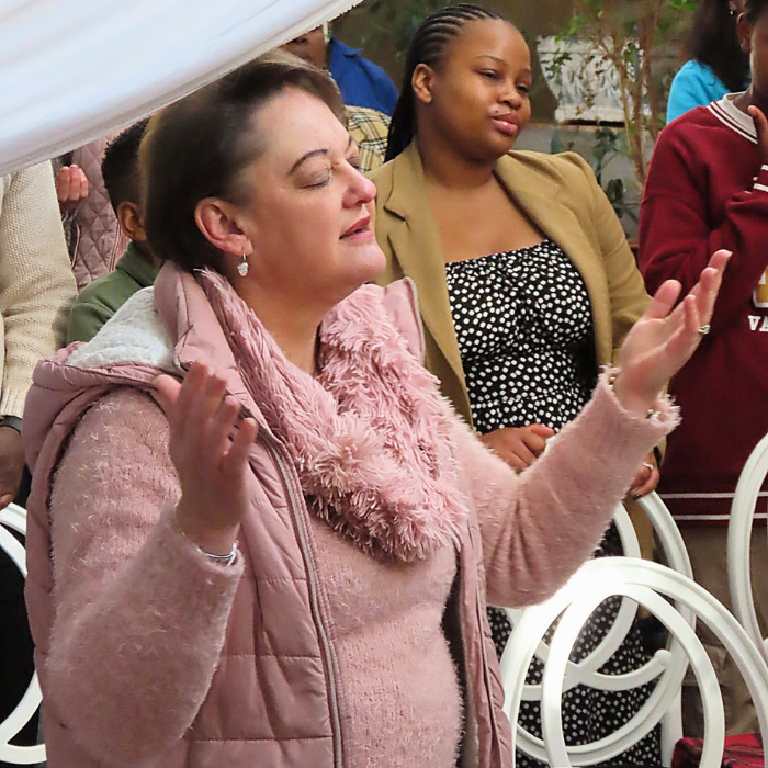 A woman with raised hands worshipping during a church service, with others around her in the background.